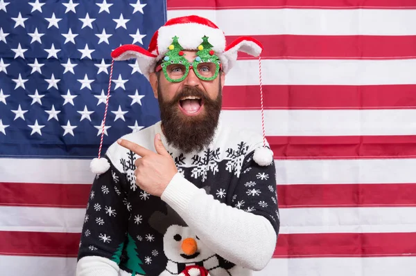 Winter is calling. Happy hipster in winter wear. Bearded man point finger at something. Enjoy winter holidays. Christmas and new year activities. Warm winter greetings. American flag background — Stock Photo, Image