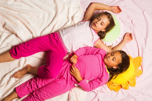 Children with sleepy faces lie close on pink blanket background