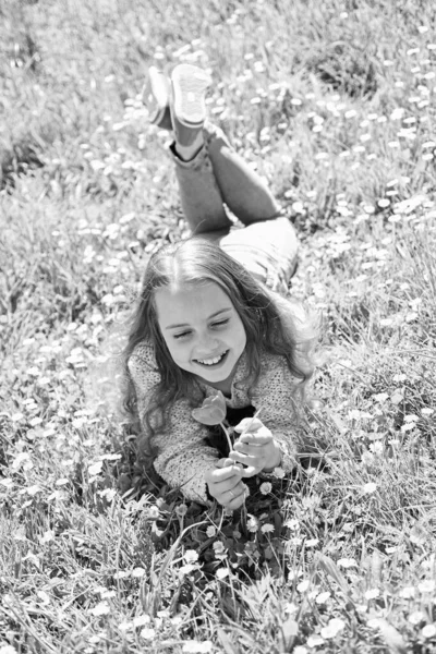 Mädchen auf Gras liegend, Graspflanze im Hintergrund. Kinder genießen den sonnigen Frühlingstag, während sie auf einer Blumenwiese liegen. saisonales Allergiekonzept. Mädchen auf lächelndem Gesicht hält rote Tulpenblume, genießt Aroma — Stockfoto