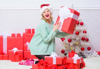 Kız arkadaş ya da eş için mükemmel bir hediye. Ona her zaman istediği hediyeyi ver. Heyecanlı sarışın, elinde fiyonklu bir hediye kutusu tutuyor. Noel hediyesini açıyorum. Noel ağacının yanındaki kız bayramı kutluyor.