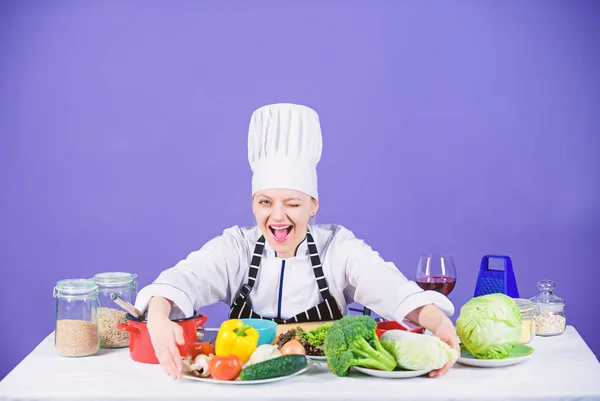Kvinna kock bära hatt förkläde nära tabell ingredienser. Flicka bedårande kock lära kulinariska. Bästa kulinariska recept att prova hemma. Hemmagjord mat tips. Förvandla ingredienser till läcker måltid. Kulinariska färdigheter — Stockfoto