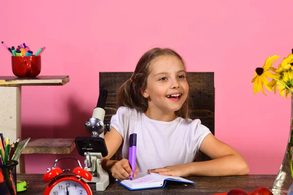 Menina senta-se na mesa com microscópio e despertador vermelho — Fotografia de Stock