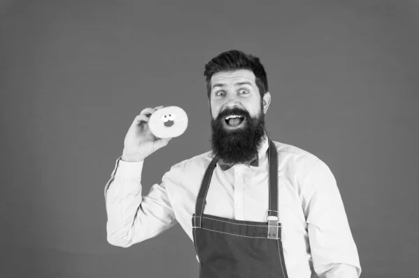 Er kocht gern. Glückliche Hipster kochen und backen gern. Profi-Koch gibt Kochkurs. bärtiger Mann in Kochschürze mit Donut auf rotem Hintergrund — Stockfoto