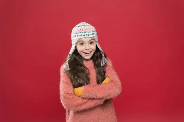 IJzig weer. Winterkleding. Schattig model genieten van de winter stijl. Klein kind lang haar dragen hoed rode achtergrond. Wintertijd concept. Kleine jongen draagt gebreide hoed. Klein meisje winter mode accessoire — Stockfoto