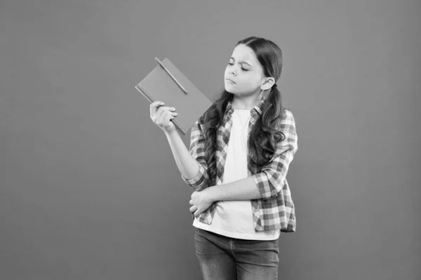 Schoolmeisje lezen boek op oranje achtergrond. ernstig klein meisje met notebook. notities schrijven. Kid Diary. literatuur les. terug naar school. poëzie en roman. modern onderwijs. middelbare school — Stockfoto