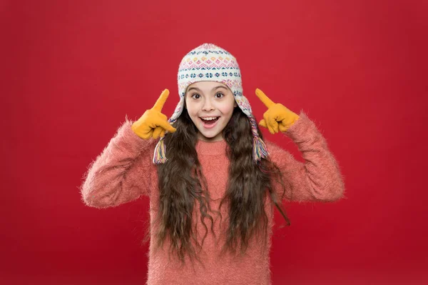 Χειμερινή έννοια. Το μικρό παιδί φοράει πλεκτό καπέλο. Μικρό κορίτσι αξεσουάρ χειμερινής μόδας. Μικρό παιδί μακριά μαλλιά φορούν καπέλο κόκκινο φόντο. Παγωμένος καιρός. Χειμερινή στολή. Χαριτωμένο μοντέλο απολαμβάνουν το χειμώνα στυλ — Φωτογραφία Αρχείου