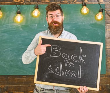 Gözlük öğretmen blackboard yazıt ile okula geri tutar. Geri okul kavramı. Sakal ve bıyık neşeli yüzü memnuniyetle öğrencilerin, kara tahta arka plan ile adam.