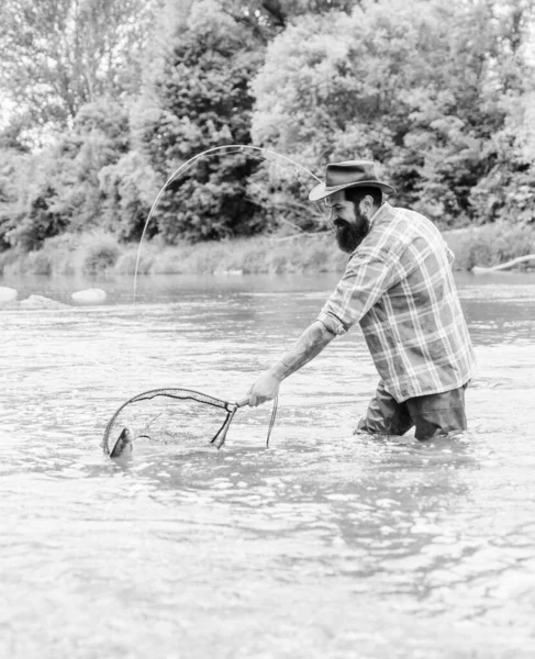 Pescador brutal barbudo captura de peces de trucha con red. La pesca es un deporte al aire libre recreativo accesible asombroso. Pasatiempo de pesca. Si los peces regularmente usted sabe lo gratificante y calmante que es la pesca — Foto de Stock