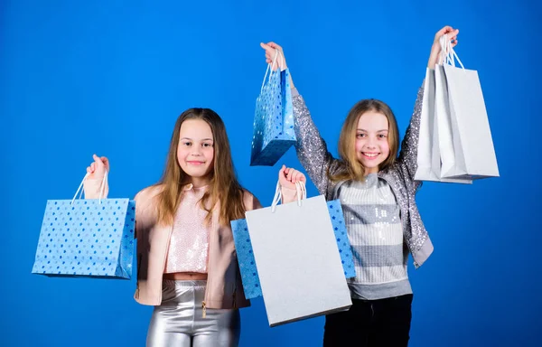 Boldog gyerekek. Kislánytestvérek. Bevásárlótáskás kislányok. Értékesítés és kedvezmények. Testvériség és család. megtakarítások vásárlások esetén. Gyerekdivat. Kék háttér. nehéz bevásárlótáskák. bevásárlótáskák. — Stock Fotó