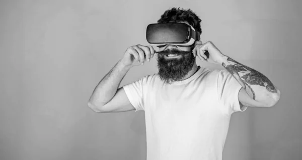 Hipster with cunning expression exploring VR with modern gadget. VR gadget concept. Man with beard in VR glasses twists mustache, green background. Guy with head mounted display interact in VR