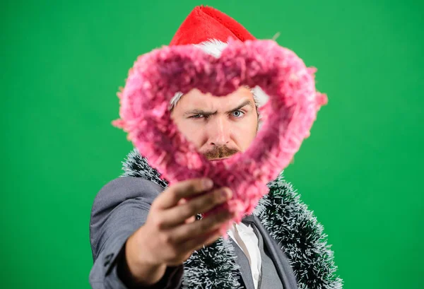 Spread love around. Merry christmas and happy new year. Hipster hold heart symbol of love. Bring love to family holiday. Man in love happy wear santa hat celebrate christmas green background — Stock Photo, Image