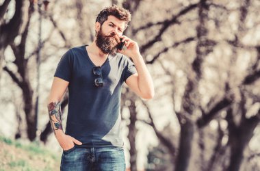 hipster adam akıllı telefon tutun. cep telefonu ile acımasız işadamı. cep telefonundan konuşan sakallı adam. konuşma ve tartışma. Sakalı olgun hipster. iş konuşması. İş uzmanları