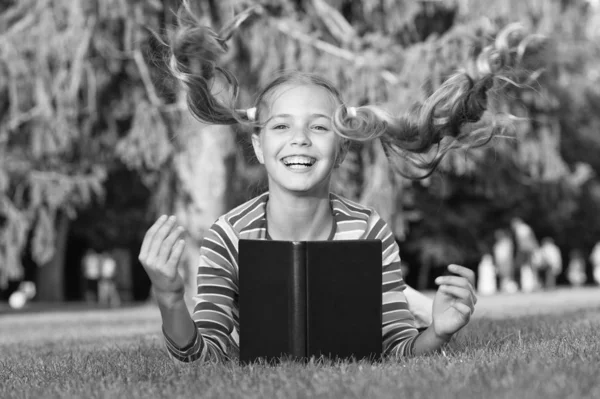 Getting your hairstyle fly. Happy child with flying hairstyle on green grass. Small cute girl smile with long tails hairstyle. Fashion look of easy hairstyle. Book knowledge. Hairdressing. Hair salon