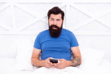 Sosyal ağları kontrol ediyorum. Hücresel iletişim. Modern adam yatakta akıllı telefondan konuşuyor. Evinden modern cep telefonu olan yakışıklı bir adam. Günlük yaşam için modern teknoloji. Modern iletişim