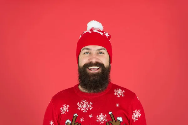 Dias frios. Férias de inverno. Homem barbudo hipster usar chapéu de malha de inverno. Barbearia e pelos faciais. Cuidados com a pele de inverno. Um tipo com roupas de inverno e acessório. Cara barbuda close up fundo vermelho — Fotografia de Stock