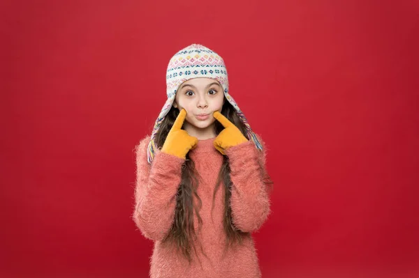 Tempo gelido. Vestito invernale. Modello carino godere di stile invernale. Il bambino indossa un cappello a maglia. Accessorio moda bambina inverno. Piccolo bambino capelli lunghi indossare cappello sfondo rosso. Cambiamento climatico — Foto Stock