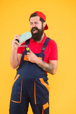 Sanayi konsepti. yaratıcı tamir konsepti. Sakallı adam paten aletinde şarkı söylüyor. Hipster mimar sarı arka planda. İş üniformalı ereksiyon asistanı. Mühendis tasarımcısı duvarı boyamaya hazır