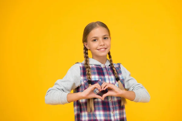 Un gesto cardiaco. Felice giornata internazionale dei bambini. Sfondo giallo bambina. Idea di buon umore. Vibrazioni positive. Emozioni sincere. Bella ragazza intrecciata. Capelli lunghi. Piccola ragazza a scacchi camicia — Foto Stock