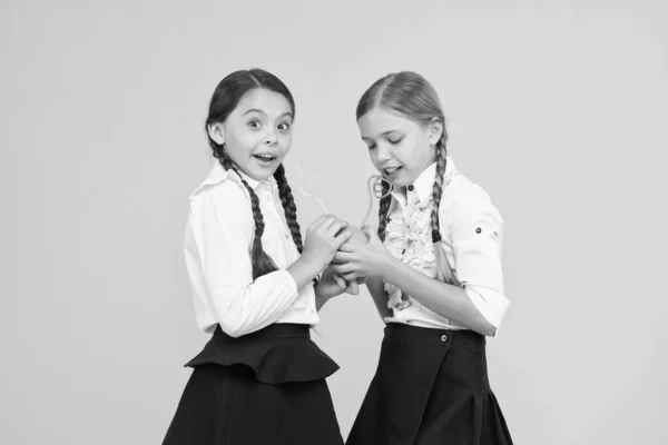 Vitamin C is crucial for the growth. Little girls drinking vitamin juice from orange fruits on yellow background. Small schoolchildren with healthy vitamin drink. Benefits of vitamin food — Stock Photo, Image