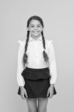 Akıllı tatlı. Sevimli küçük kız sarı arka planda gülümsüyor. Okul üniforması giyen mutlu küçük bir kız. Uzun örgülü örgülü saçlı ilkokul kızı. Sevimli kız gurur bir öğrenci olmak
