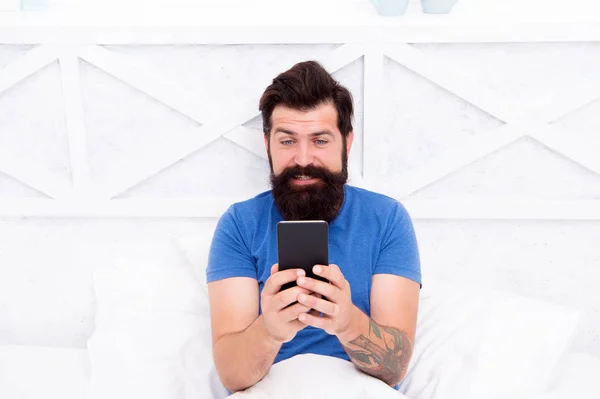 Concepto de videollamada. Comunicación celular. Tipo moderno hablando en el teléfono inteligente en la cama. Hombre guapo con teléfono móvil moderno desde casa. Tecnología moderna para la vida cotidiana. Comunicación moderna —  Fotos de Stock