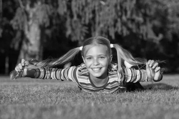 Glad Schoolgirl på solig dag. Glad leende elev. Ha det så kul. Flicka unge om grönt gräs. Friska känslomässiga Happy Kid avkopplande utomhus. Flicka ponytails frisyr njuta av avkoppling. Living Happy Life — Stockfoto