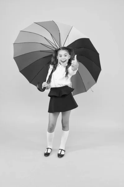 Divattudás. Boldog iskolás a divat meg, amely remek a sárga háttér. Kisgyermek gazdaság szivárvány színű divat esernyő. Kis divat gyerek élvezi iskolája öltözködési — Stock Fotó