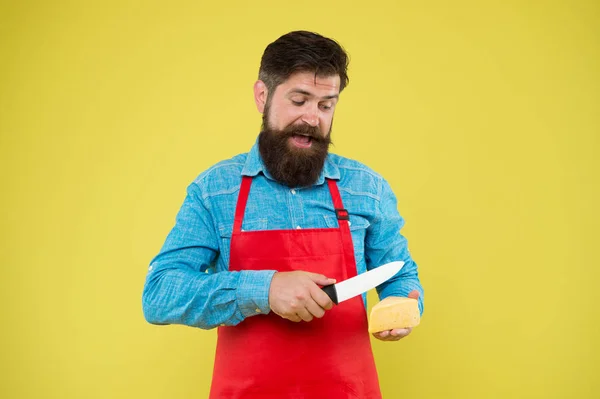 Professionellt kök koncept. Ostfestival. Föda och näring. Glad skäggig man skuren ost med kniv. Osttillverkning. Osttillverkare äger företag. hipster med skägg i köksmästare förkläde. Mjölkaffär — Stockfoto