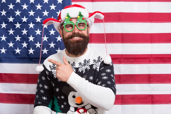 Hey look. Happy hipster point index finger at something. Bearded man point and laugh. American flag background. Point gesture. Advertising point. Merry Christmas. Happy new year