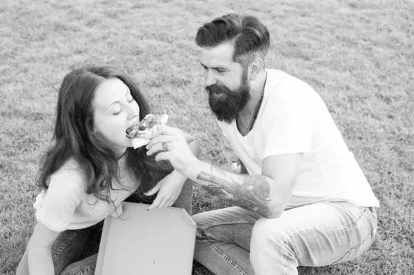 Pizza tid. sommar picknick på grönt gräs. familjehelg. par i kärlek dating. Snabbmat. skäggiga man hipster och bedårande flicka äter pizza. lyckligt par äter pizza. utfodring hans flickvän — Stockfoto