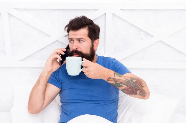 Pleasant conversation. Good morning. Modern life new technology. Technology concept. Hello dear. Bearded man using mobile technology in bed. Handsome guy talking on phone and drinking coffee at home