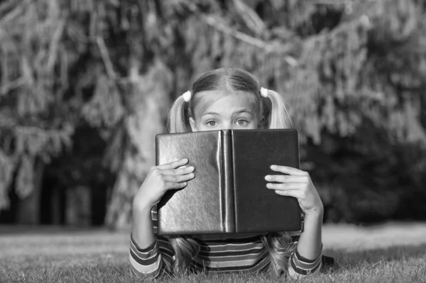 Nesuď knihu podle obalu. Rozkošná dětská obálka s knihou. Roztomilá holčička čte knihu o zelené trávě. Skvělé oko pro dobrou knihu — Stock fotografie