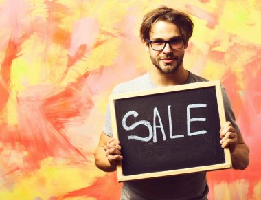 Beyaz sakallı seksi maço adam elinde satılık bir yazı tutuyor.