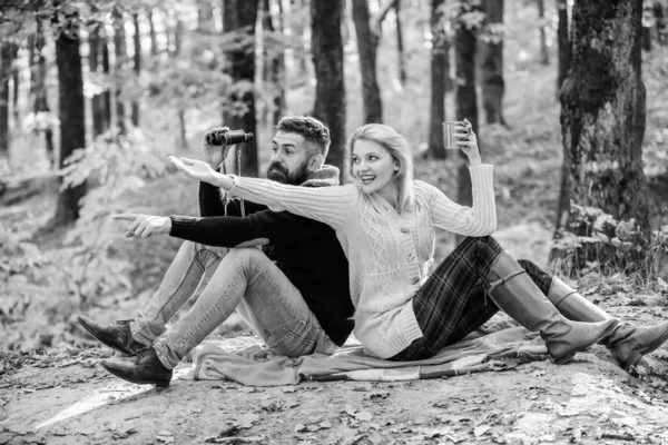 Titta där. Koppla av i parken tillsammans. Happy Loving par koppla av i parken tillsammans. Par i kärlek turister avkopplande picknick filt. Man med kikare och kvinna med metall mugg Njut av naturparken — Stockfoto