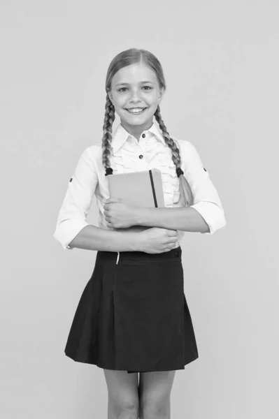 Essere orgogliosa della sua conoscenza. Piccolo bambino carino con conoscenze scolastiche in mano. Adorabile piccola ragazza che tiene libro su sfondo giallo. Conoscenze e competenze. Giorno della conoscenza o 1 settembre — Foto Stock