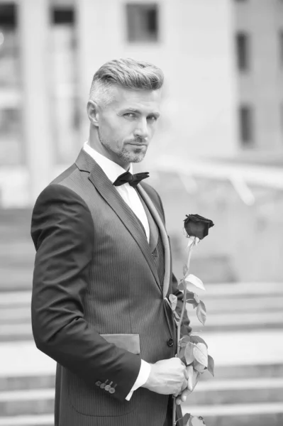 Make good first impression. Valentines day and anniversary. Handsome guy rose flower romantic date. Well groomed macho tailored suit. Romantic gentleman. Man mature confident macho with romantic gift