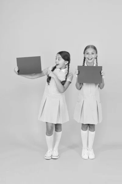 A fornecer novas informações. Anúncio e promoção. Alunos alegres de alunas informando você. Meninas uniforme escolar segurar cartazes. De volta à escola. Escola meninas segurar espaço de cópia de papel em branco — Fotografia de Stock