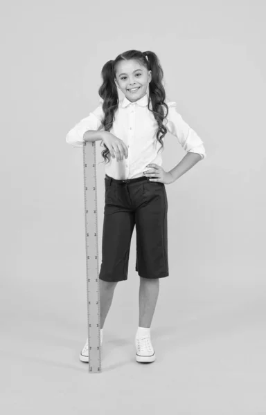 Es hora de aprender. Niño de escuela pequeña con reglas que aprenden matemáticas y geometría sobre fondo amarillo. Niña aprendiendo medidas de longitud en la escuela. Aprendizaje y educación — Foto de Stock