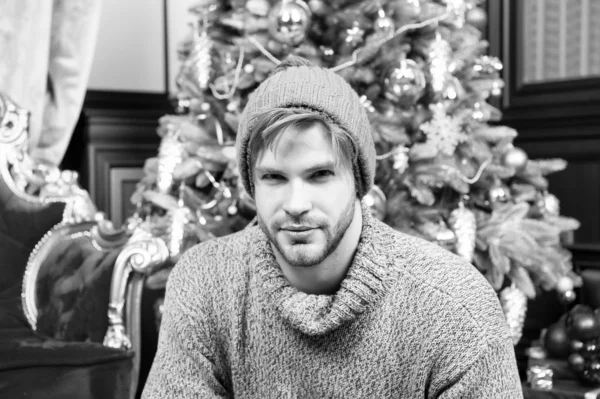 Guy v teplou čepici, svetr sedí u vánočního stromu — Stock fotografie