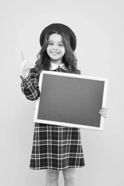 Bulletin board. parisian child on yellow backgrounf with bulletin board. copy space. advertisement. child with empty blackboard. happy girl with long curly hair in beret. small girl in french beret — Stock Photo, Image