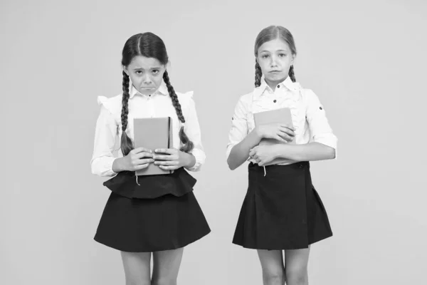 Unhappy bookworms. Unhappy little schoolchildren on yellow background. Adorable small girls with unhappy emotions holding books. Unhappy because of bad marks — Stock Photo, Image