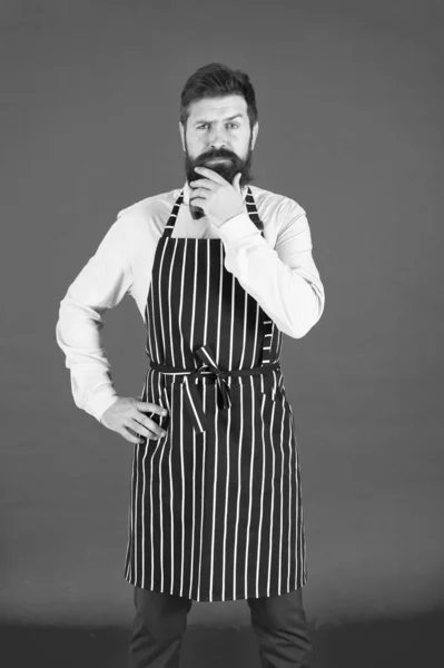 Thinking about new recipe. Elegant waiter man or bartender. Bearded man wearing bib apron. Man cook with beard and mustache in cooking apron. A thoughtful man servant — Stock Photo, Image
