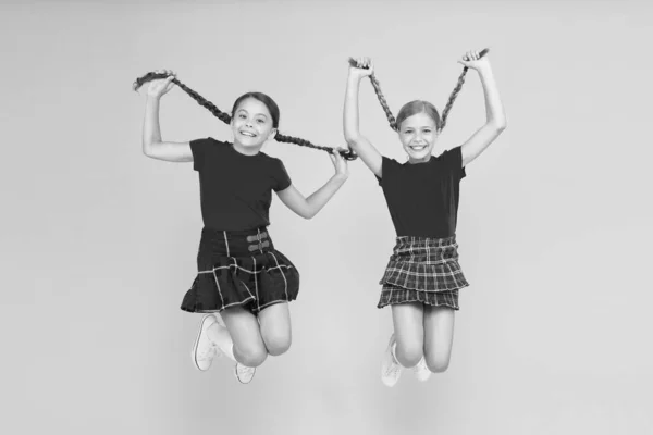 Känsla lekfull. skönhetslook. lyckliga barn på gula muren. barndoms glädje. trendig skoluniform. roligt hopp. röda mode flickor. engelsk stil mode. lyckliga små flickor i rutig kjol — Stockfoto