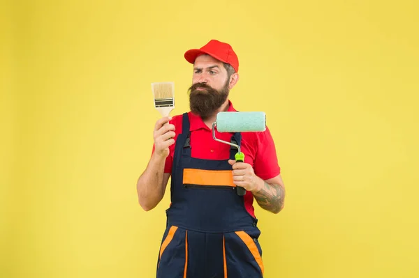 Reparatur und Renovierung. Bauarbeiter halten Farbroller und Pinsel in der Hand. perfekte Oberflächenbemalung. Vinylfarbe auftragen. Pick-Ups. Malwerkzeug. Pinselwalzenmaler. Mann bärtige Arbeiter Malerei — Stockfoto