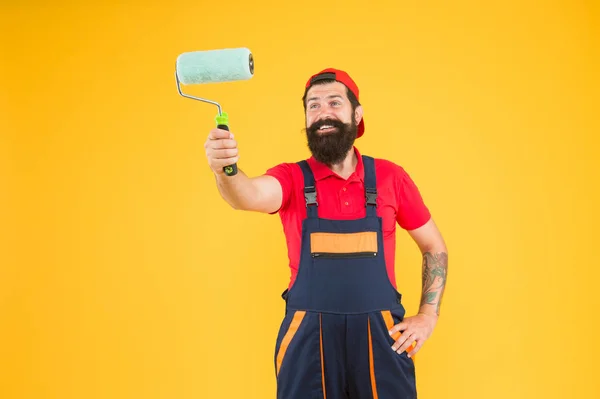 Schilderwerk. reparatieassistent in werkuniform. ingenieur ontwerper klaar om muur te schilderen. reparatieconcept. gelukkige man met baard en roller tool. hipster bouwer in cap gele achtergrond — Stockfoto