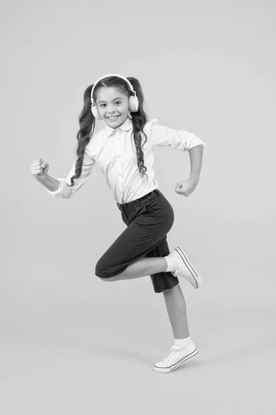 Energetic back to school songs that will get you moving. Energetic child is hurrying to school on yellow background. Small girl enjoying energetic music in earphones. Active and energetic — Stock Photo, Image