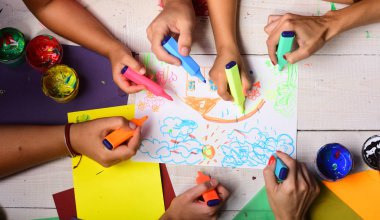 Eller renkli kalemleri tutar ve çocukların resimlerini çizer.