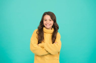 Moda senin kadar eşsiz. Mutlu çocukluk. Uzun esmer saçlı küçük bir kız. Çocuk sıradan kış modası tarzında. Küçük kızın saf güzelliği. Çocuklar için örgü örüyorum. Mavi arka planda küçük bir kız