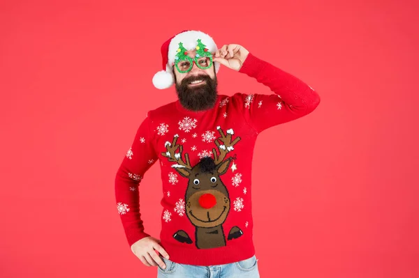 Geef een grote chee. grappige hipster gebreide trui. breimode. wintervakantie viering. Baard man kerstman hoed rode muur. Kerstmis is hier. Een man met een kerstbril. Gelukkig nieuw jaar 2020 — Stockfoto