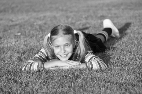 Living happy life. Cheerful schoolgirl on sunny day. Happy smiling pupil. Have fun. Girl kid laying green grass. Healthy emotional happy kid relaxing outdoors. Girl ponytails hairstyle enjoy relax
